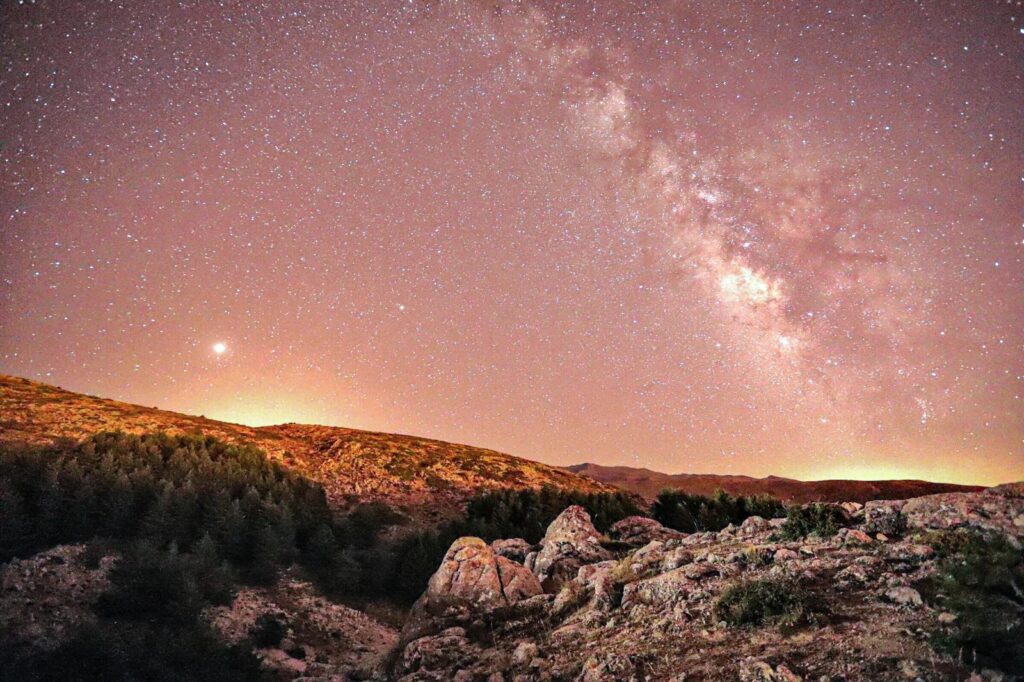 Starry night over the rugged mountains, with the Milky Way stretching across the sky in Sierra Nevada. The landscape glows under the soft light, capturing the beauty of astrophotography in a remote, unspoiled setting.