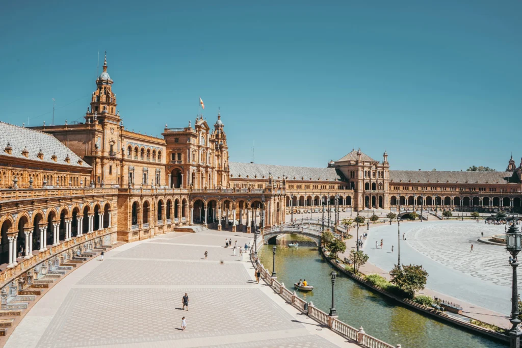 Plaza de España, Seville – A grand semicircular plaza with Renaissance Revival and Moorish architectural influences, featuring an ornate bridge over the canal, ceramic-tiled details, and the impressive central building bathed in sunlight.