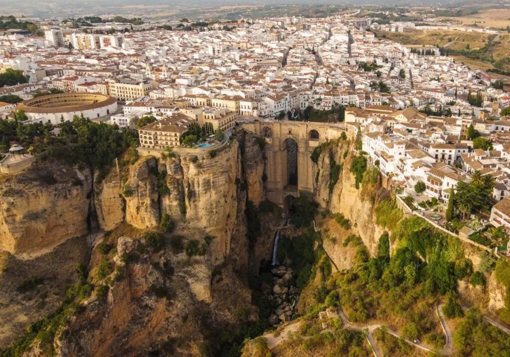 Aerial view of Ronda, Spain, showcasing the iconic Puente Nuevo spanning the deep El Tajo gorge. The historic town’s whitewashed buildings, bullring, and dramatic cliffs create a breathtaking Andalusian landscape.